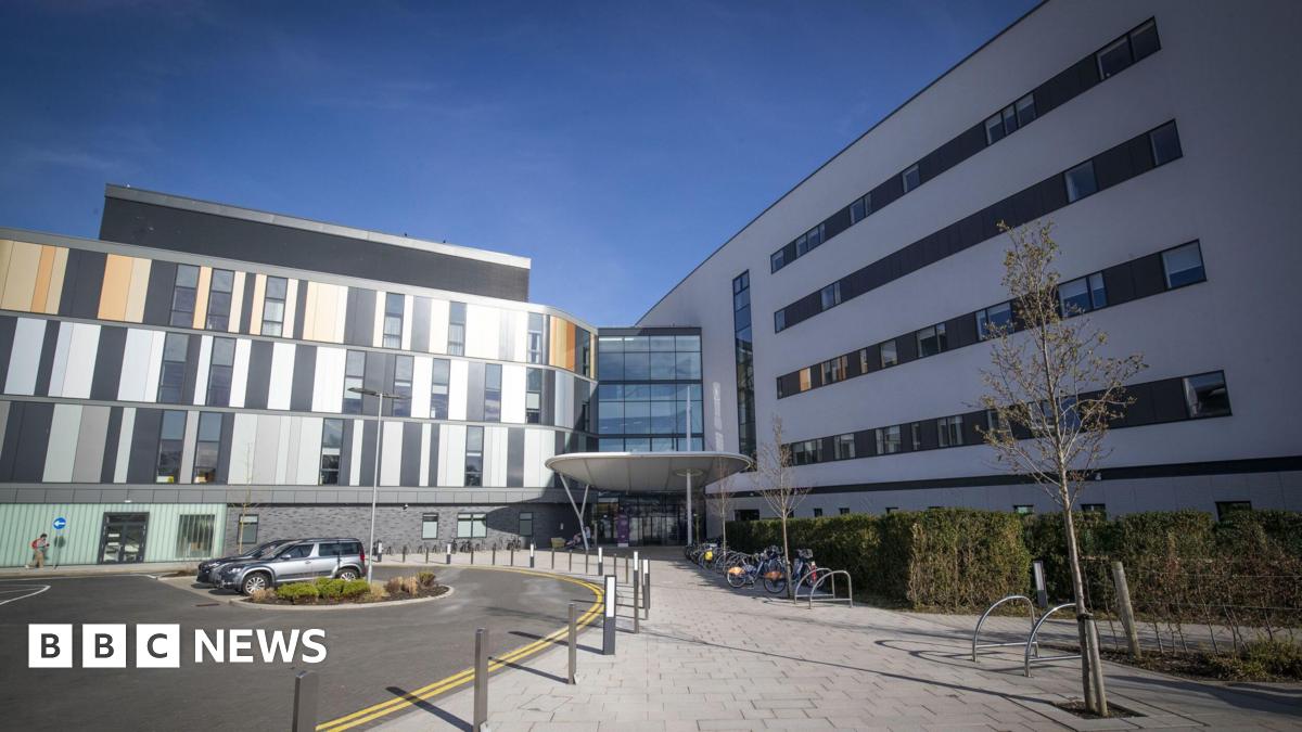 general view of the main entrance to the Royal Hospital for Children and Young People Edinburgh, a modern hospital building with sections of dark grey and light grey panelling and windows. There is a bike rack at the front and a road curves by the entrance