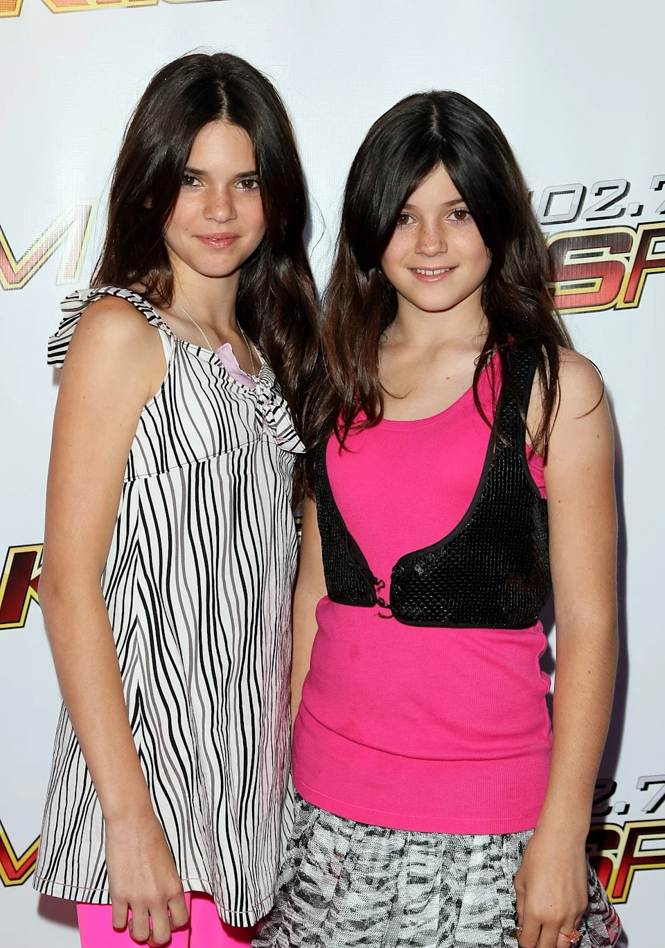 Kendall Jenner is wearing a striped top, and Kylie Jenner is wearing a pink top with a black vest and a patterned skirt