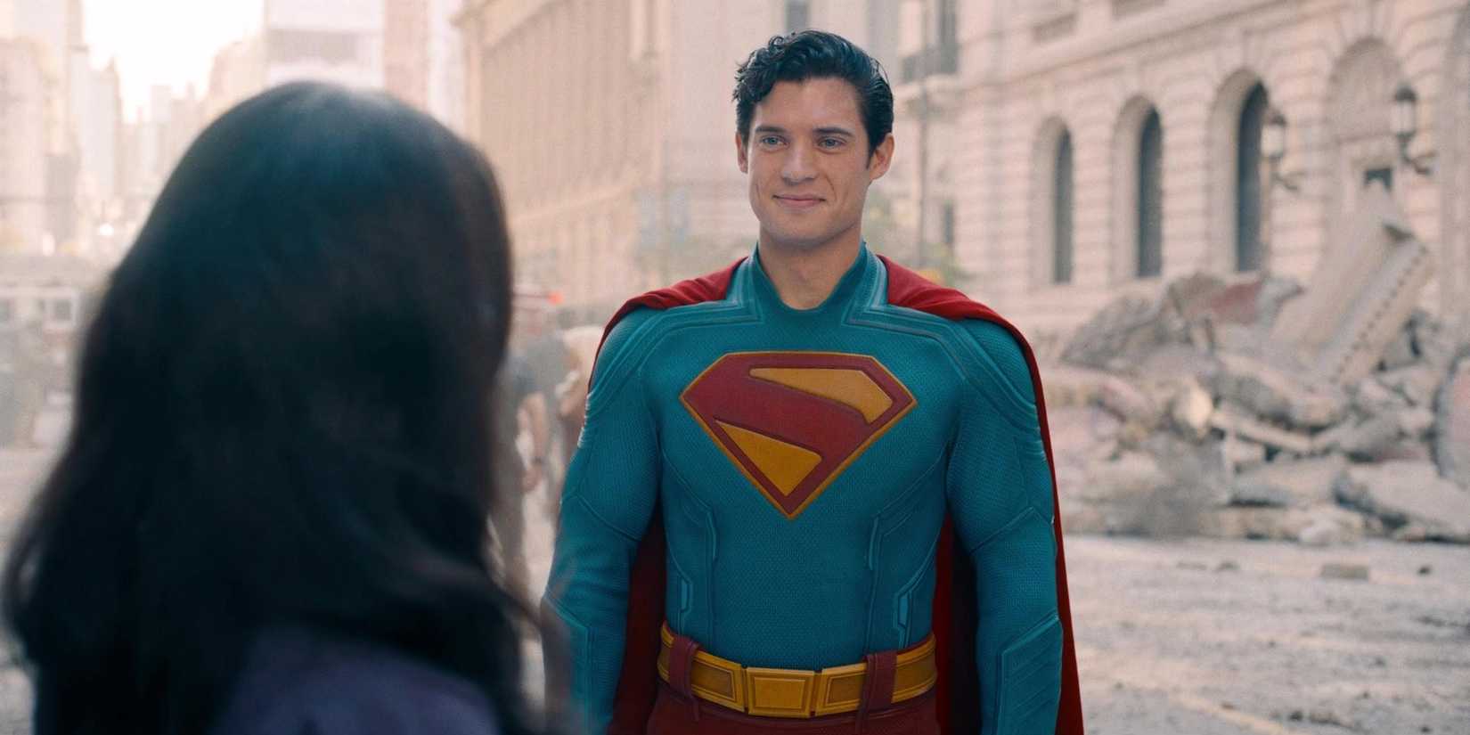 David Corenswet's Superman smiling while looking at Rachel Brosnahan's Lois Lane in Superman (2025) with Metropolis partly destroyed in the background
