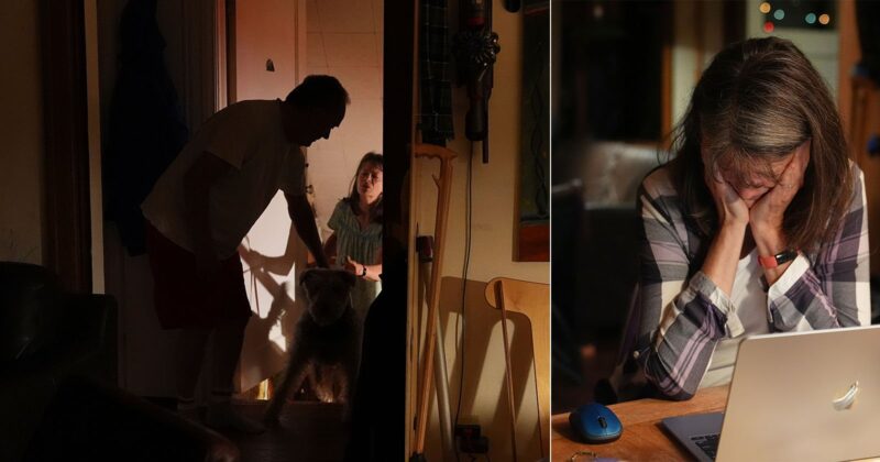 A dimly lit home scene split in two: on the left, a man and a woman greet a dog at the door; on the right, the woman sits at a table, looking down with her head in her hand beside an open laptop.
