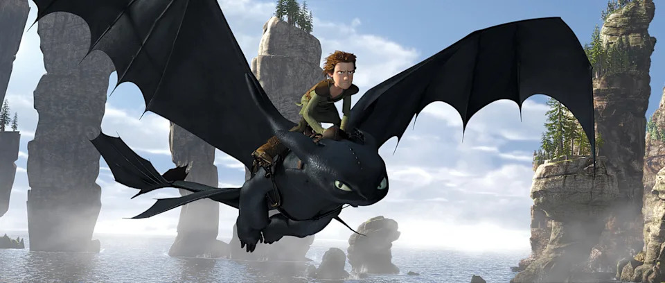 A person riding a large, flying dragon over a scenic, rocky coastline with tall rock pillars in the background