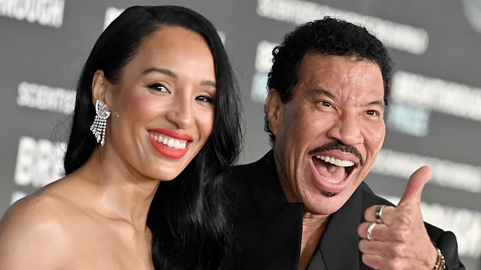 Lisa Parigi smiles on the red carpet while Lionel Richie flashes a thumbs up right next to her at the 9th Annual Breakthrough Prize Ceremony