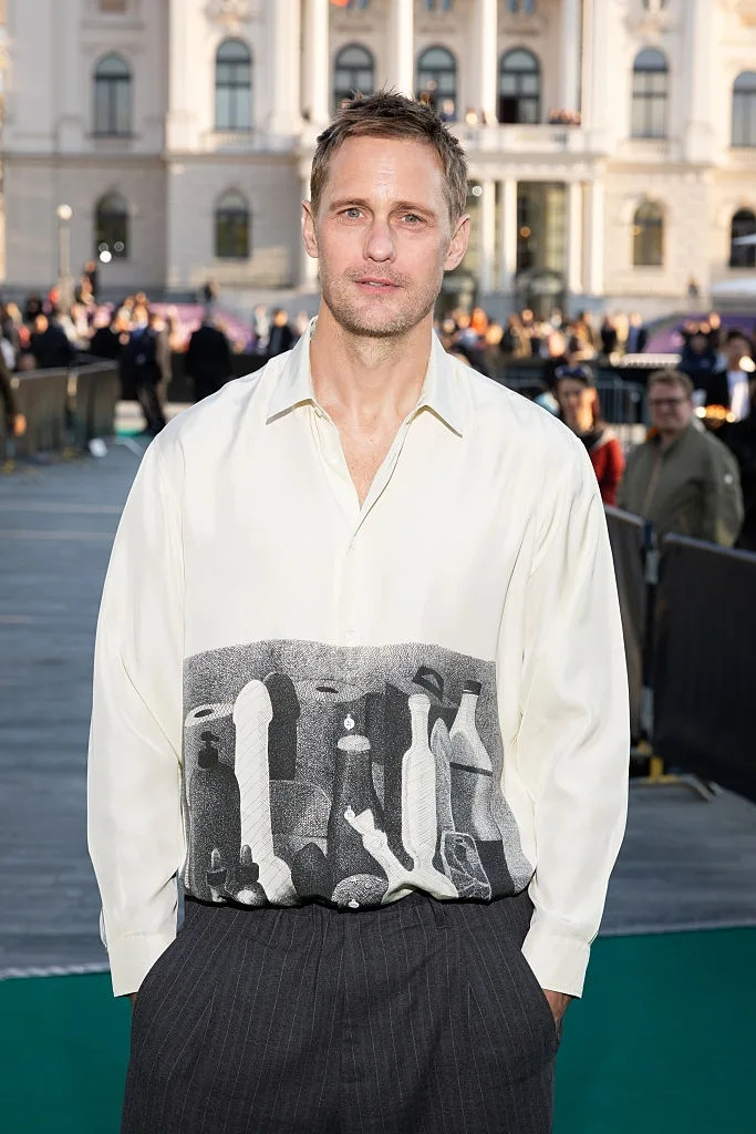 A man in a patterned button-up shirt and pin-striped pants poses outdoors at an event