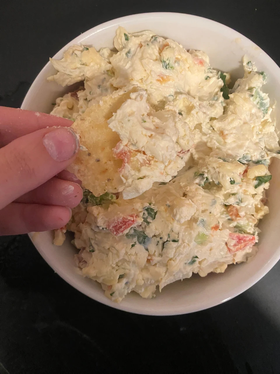 A bowl of creamy vegetable dip being scooped with a tortilla chip by a person's hand