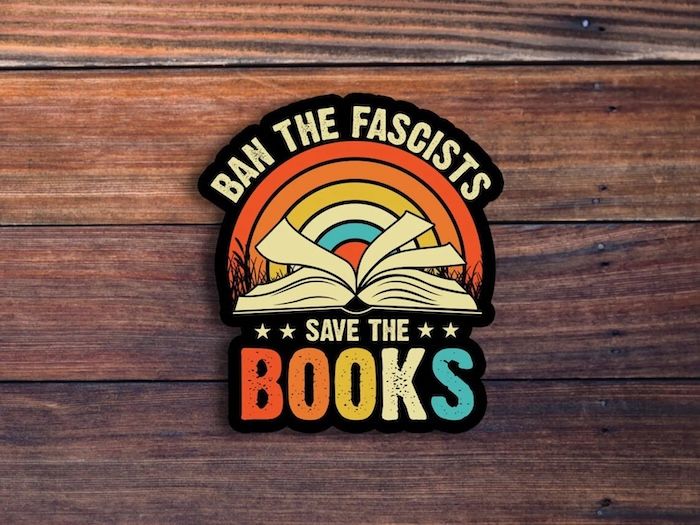a sticker that says Ban the Fascists Save the Books. the text borders an open book in front of a rainbow
