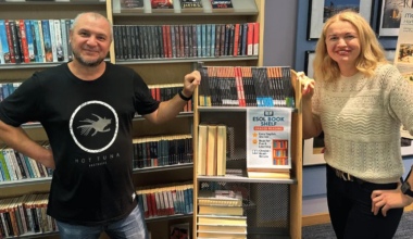 A man and a woman standing next to book shelves.