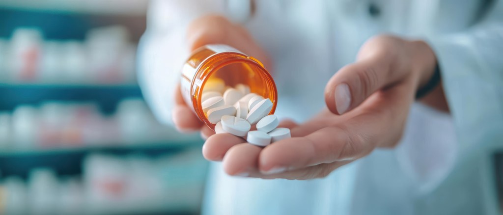 A pharmacist dispensing white pills from a bottle into their hand.
