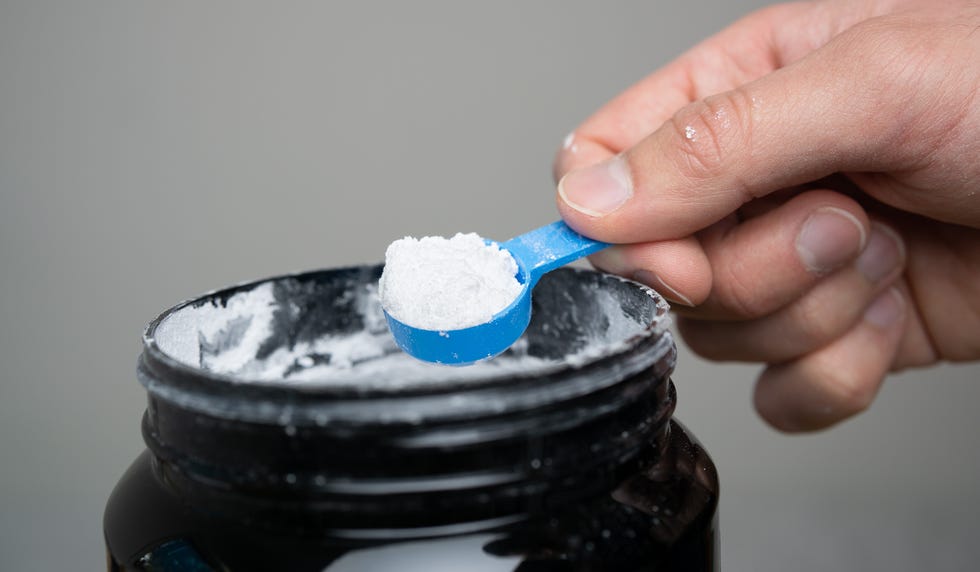 close up of man hand holding measuring scoop of creatine