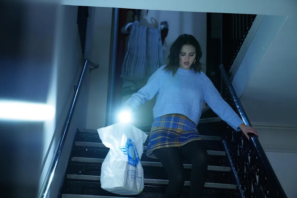 Selena Gomez descends stairs holding a flashlight and a plastic bag in a scene from "Only Murders in the Building."