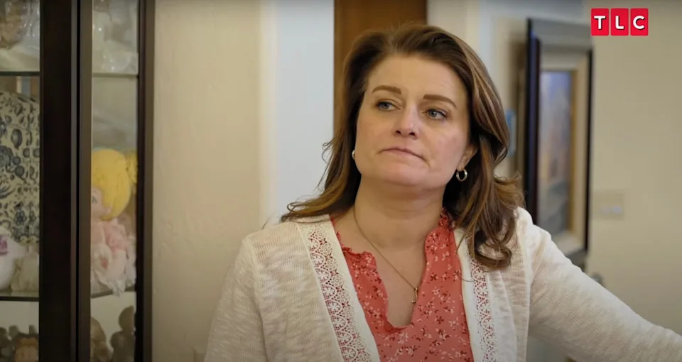 Robyn Brown wearing a coral blouse and cream cardigan, looking serious during a scene from Sister Wives.