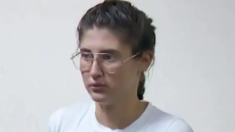 Rustavi 2 Bella Culley filmed in court. She is wearing glasses and has brown hair in a plait and is wearing a white top