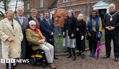 A group of people standing next to a brick-built sculpture showing the partial face of Josiah Wedgwood with a building visible behind.