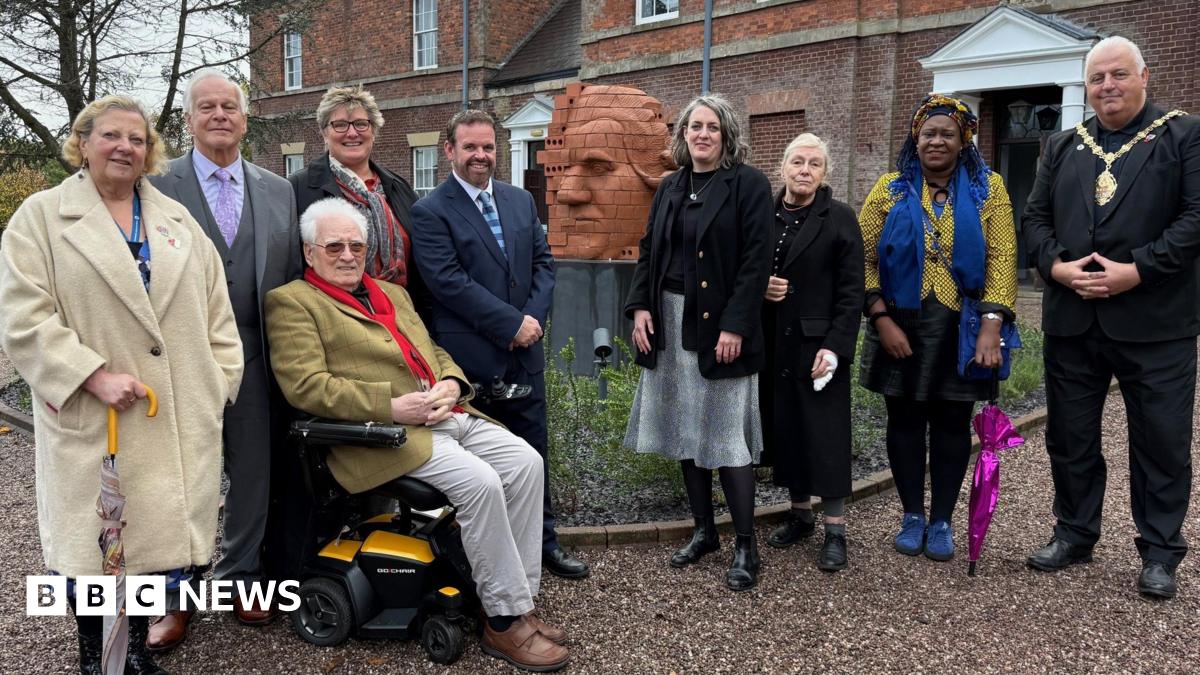 A group of people standing next to a brick-built sculpture showing the partial face of Josiah Wedgwood with a building visible behind.