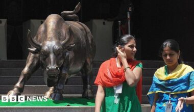 Indian women walk past the bronze bull outside the Bombay Stock Exchange, wearing traditional salwar-kurtas.