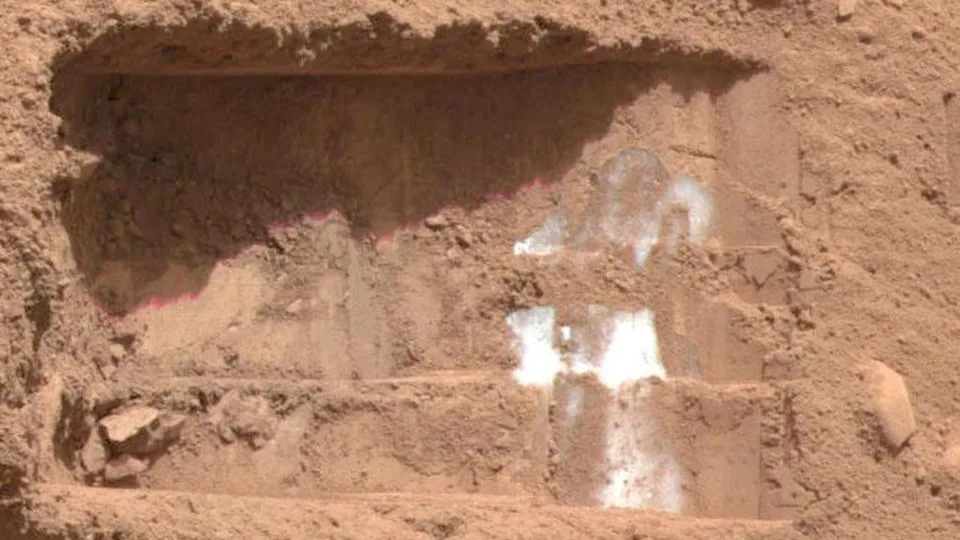  A close up of a the reddish-brown surface of Mars with white streaks across it. 