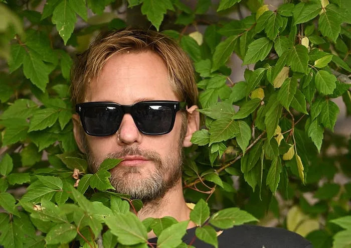 Man wearing sunglasses surrounded by leafy branches