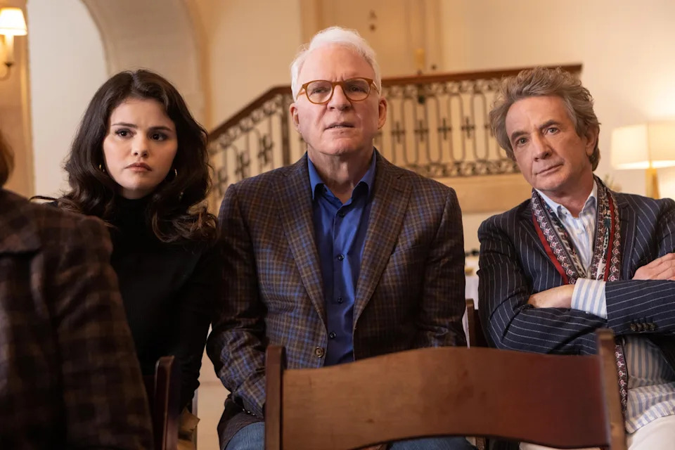 Selena Gomez, Steve Martin, and Martin Short are seated and looking ahead seriously in a scene from "Only Murders in the Building."