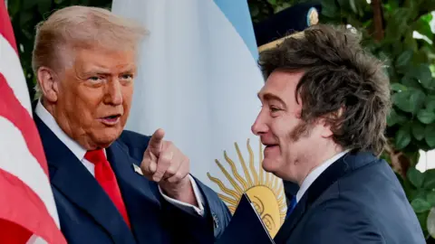Reuters Two men wearing suits stand in front of the American and Argentinian flags. One man points toward the camera.