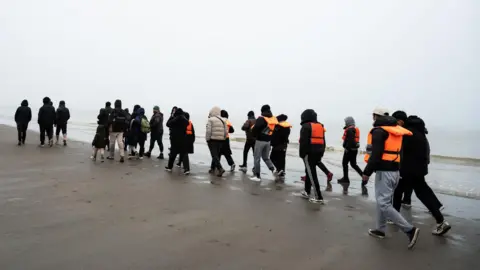 Getty Images A group of migrants, some wearing lifejackets walk along a beach in France before taking a boat to the UK.
