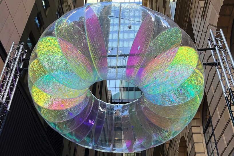 floating oculus installation shimmers in shifting chromatic light above brooklyn's streets
