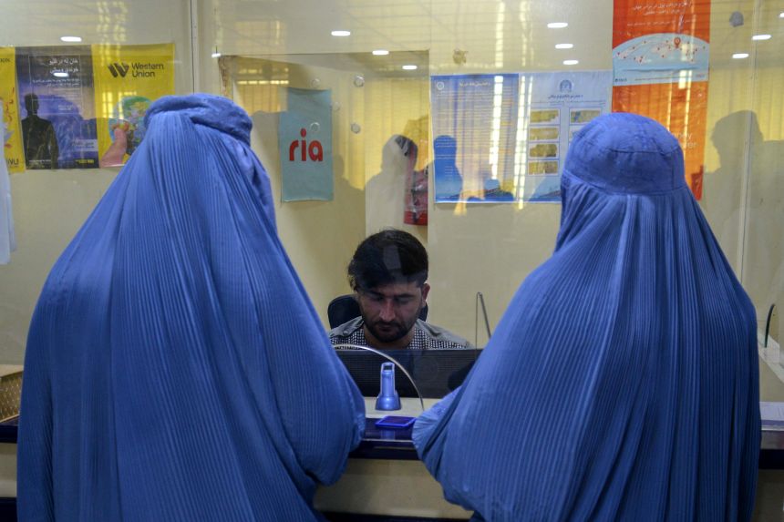 Afghan women wait at a counter to withdraw money inside a bank in Kandahar.