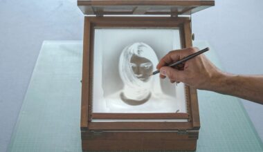 A hand holding a pencil traces over a photographic negative of a woman's face, which is placed inside a wooden box with a glass lid. The box sits on a green cutting mat.