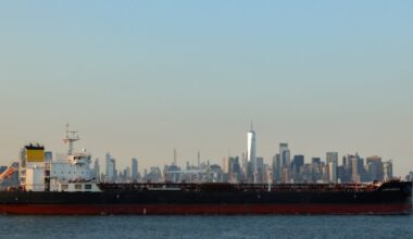 A large cargo ship leaves Port Jersey Container Terminal with the Manhattan skyline visible in the background.