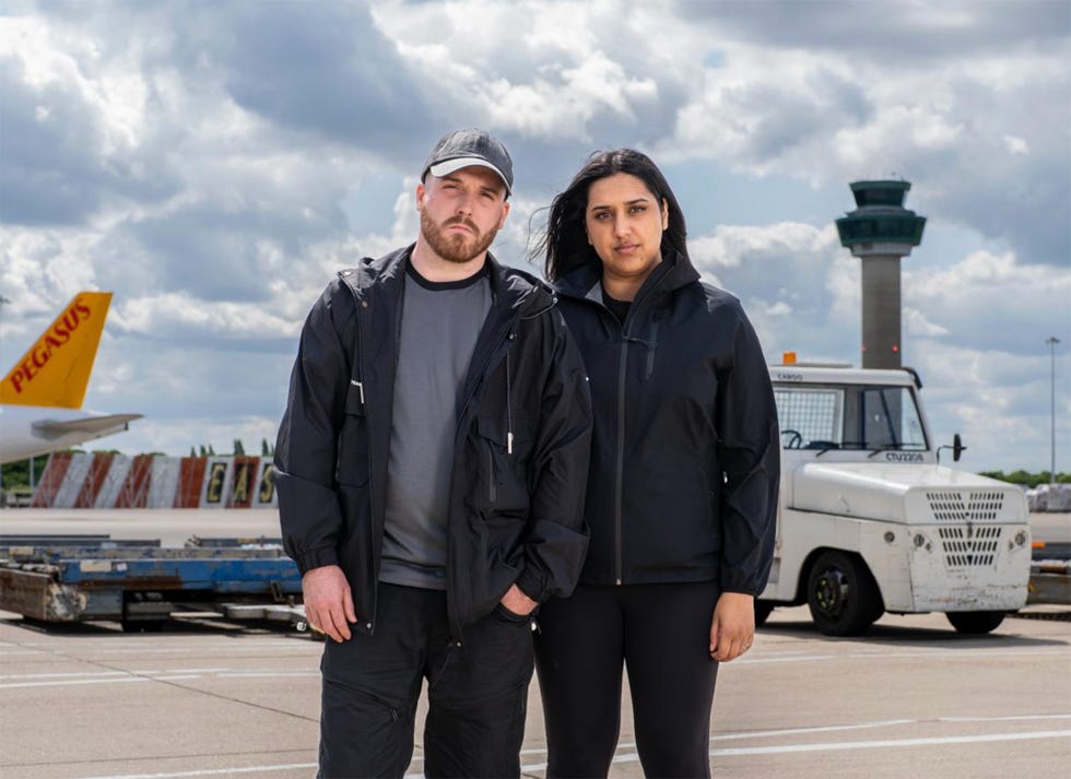 Hunted 2025 contestants Cameron and Simran two individuals standing on an airport tarmac with an air traffic control tower in the background and a cargo vehicle nearby