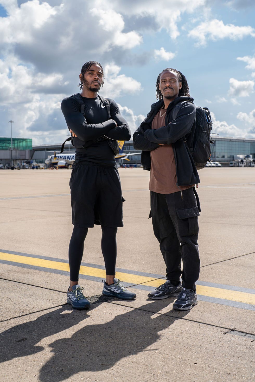 Hunted 2025 contestants Shaq and Warren two individuals standing on an airport tarmac with arms crossed