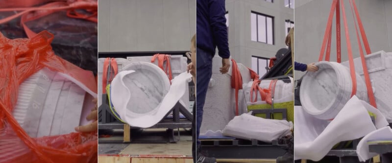 Four photos show the unpacking and installation of a large marble washing machine sculpture, with workers removing red straps and plastic wrap around the artwork outside a building.