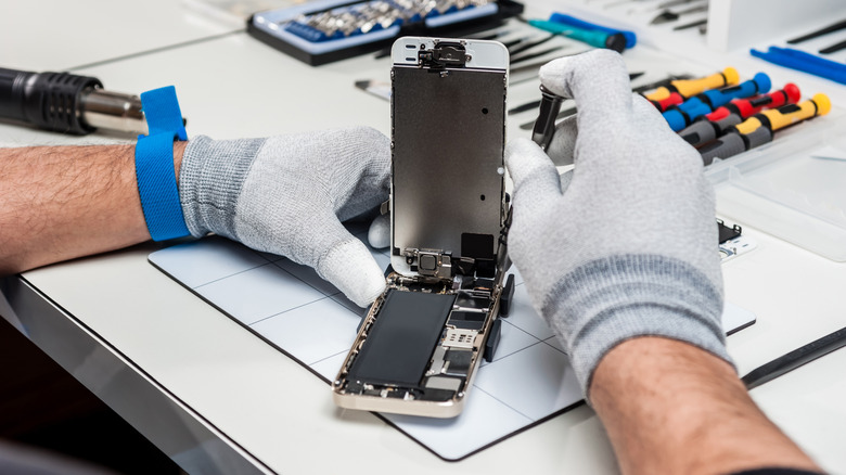 Smartphone being repaired by gloved hands on table