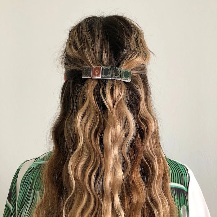 person with a half-up hairstyle with a barrette made of five small books in their hair