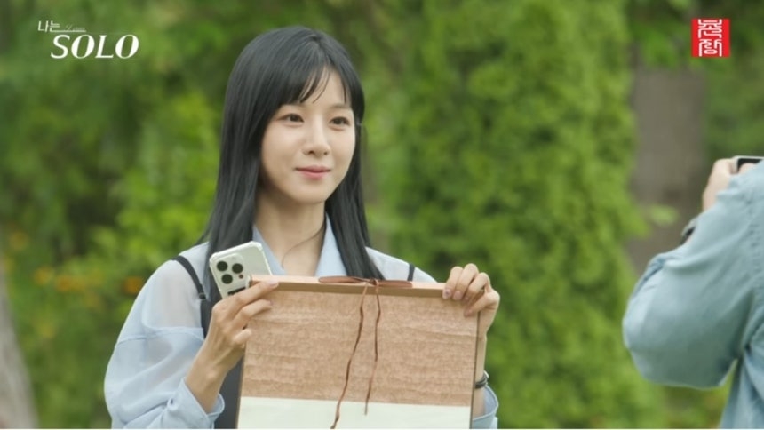 A contestant on "I'm Solo" shows her name written on a scroll to the other person. (SBS)
