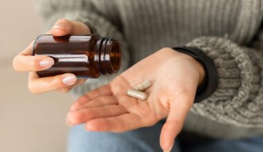 A person pouring beige capsules into their hand while wearing a grey knit sweater.