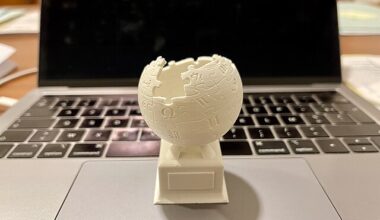 A 3D-printed version of the Wikipedia logo rests on the touchpad of an open MacBook.