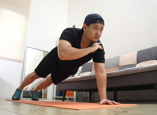 Asian male doing exercise at home to stay healthy on new normal lifestyle, indoor home workout concept, shoulder tap push ups plank position