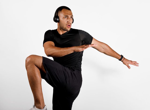 Sporty African American Man Doing Elbow To Knee Crunch Exercise And Listening To Music, Wearing Wireless Headphones On White Studio Background. Fitness Workout Playlist. Panorama, Copy Space