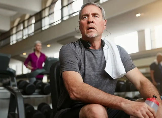 Fitness, break and tired senior man at a gym with water after training, exercise or challenge. Sports, fatigue and elderly male person with liquid for hydration, recovery or resting from workout