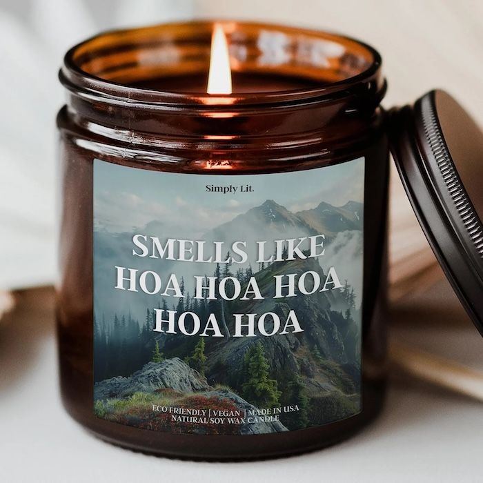 an amber candle jar with a printed label on the front of a mountain range and foggy sky with text that reads Smells Like Hoa Hoa Hoa Hoa Hoa.