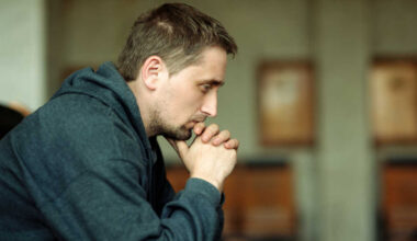 A man sitting down, leaning his head on his hands, worried.