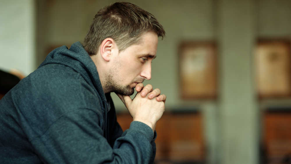 A man sitting down, leaning his head on his hands, worried.
