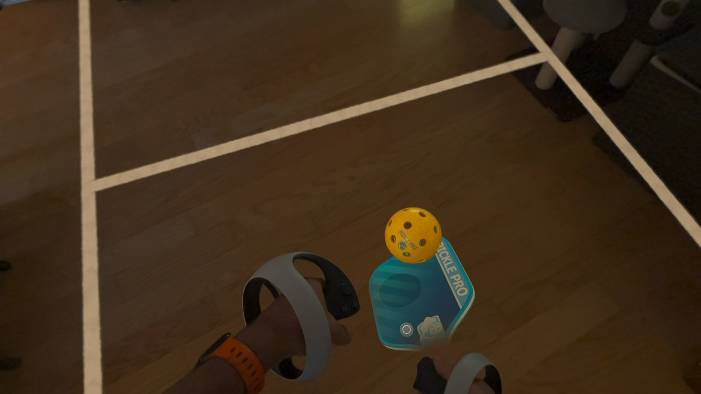 A person wearing VR headsets and controllers playing a virtual pickleball game on a wooden floor.