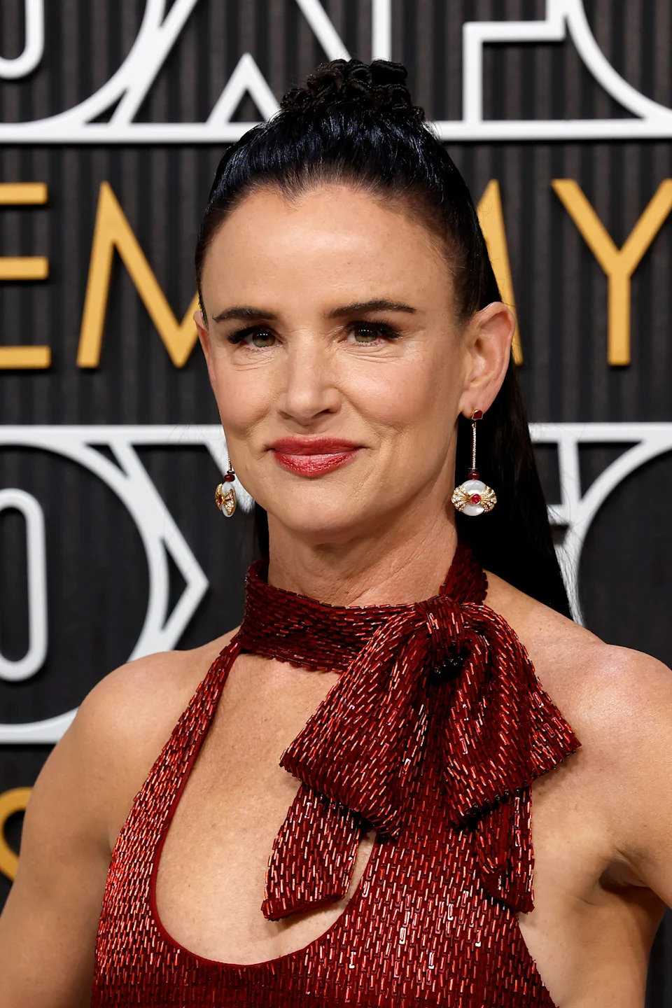 Actress in a shimmering, sleeveless dress with a high neck and bow detail on a red carpet event