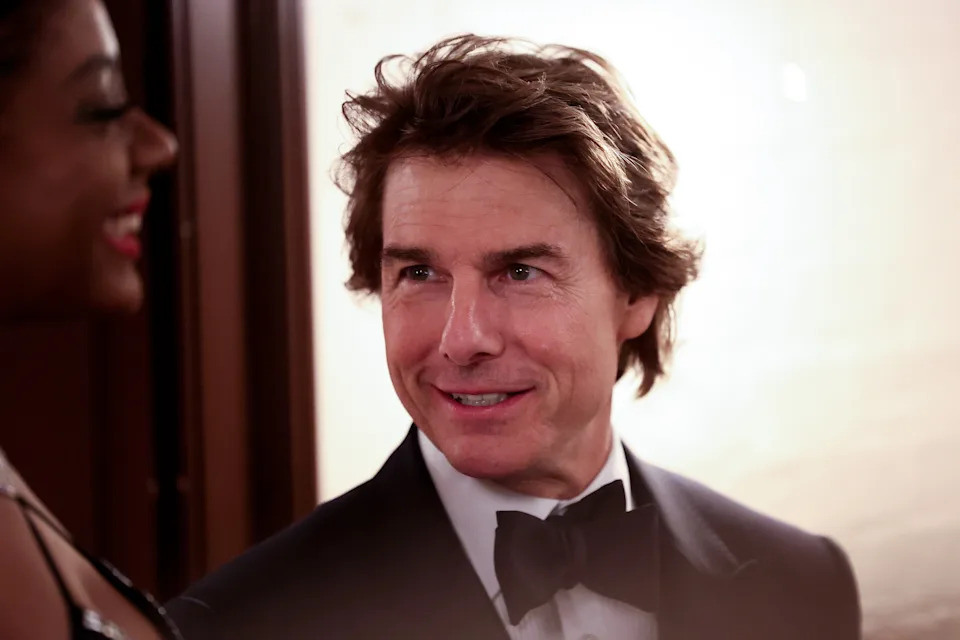 A person in a tuxedo smiles while talking to someone at a formal event