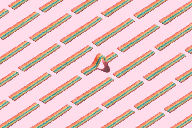 A Curved Rainbow Striped Candy Standing Out Form the Crowd on Solid Pink Colored Background.