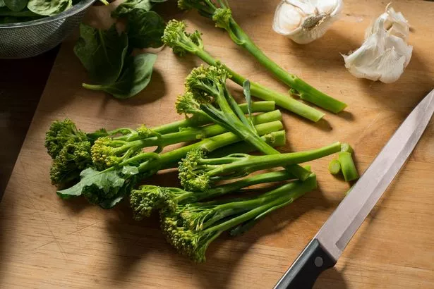 Tenderstem broccoli, garlic, and a sharp knife on a wooden board.