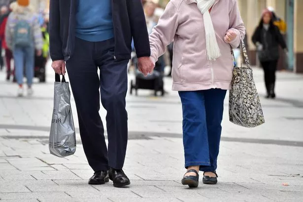 Pensioners out shopping holding hands as they walk along the road 