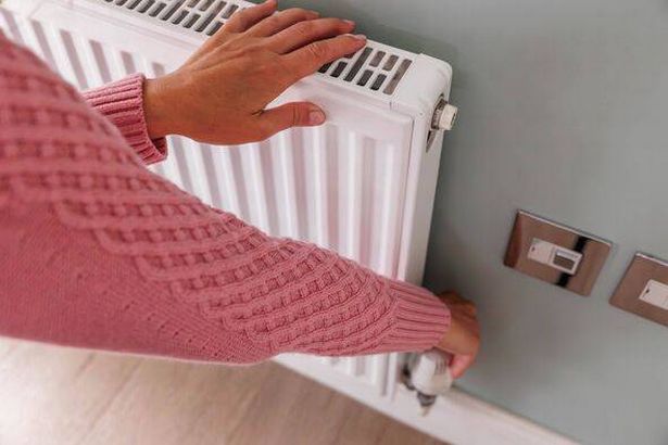 Top view of woman's hands in a wool pink jumper turning down the heating temperature on a home radiator using a thermostat. Ener