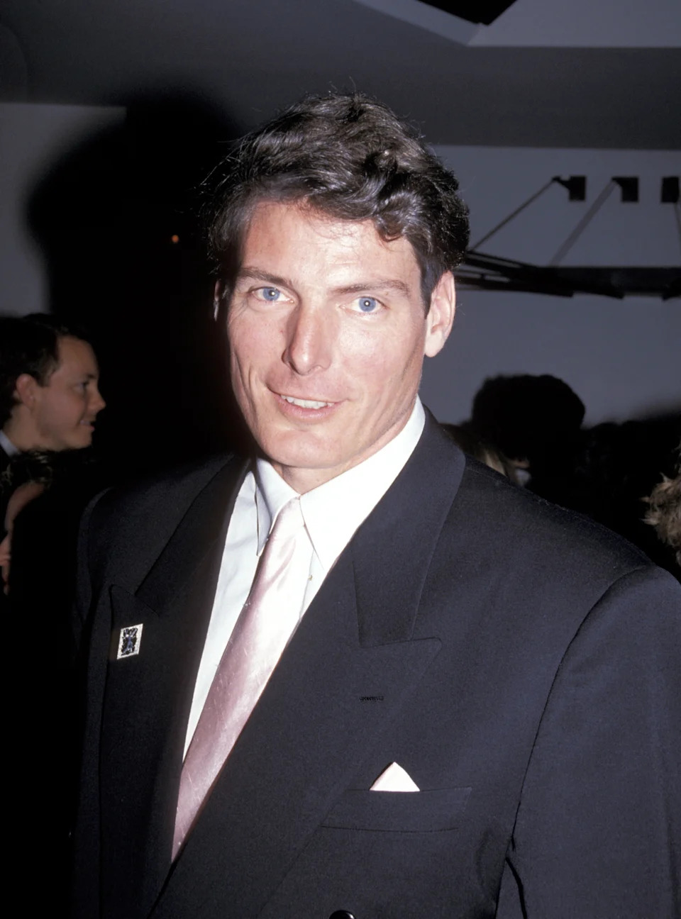 A person in a formal suit with a light tie at an event, looking at the camera