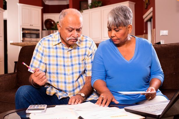 A man and woman are sitting on a sofa looking at paperwork 